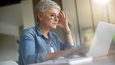 mujer mayor mirando un ordenador mientras se lleva una mano a la cabeza