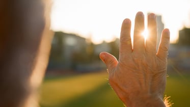 Persona mayor con la mano levantada viendo el atardecer